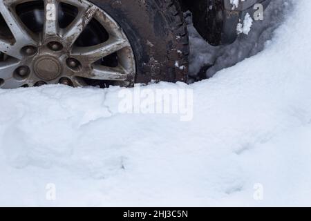 Ein schmutziges Autorad klemmte auf einer schneebedeckten Straße. Schnee driftet im Winter. Stockfoto