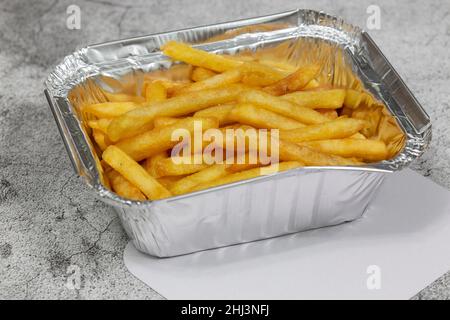 Pommes frites in einem Tablett mit Deckel zum Mitnehmen. Auf einem konkreten Hintergrund Stockfoto