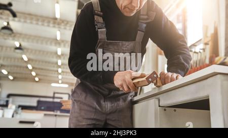 Nahaufnahme der Tischlerhände beim Polieren von Holzplatten mit Schleifpapier in der Werkstatt. Horizontale Aufnahme. Zugeschnittenes Bild Stockfoto