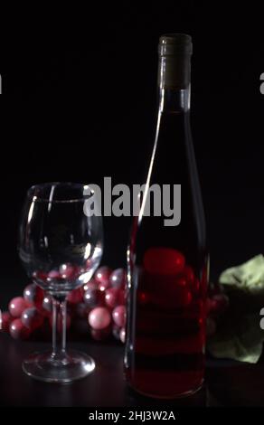 Flasche Rotwein kein Etikett mit Requisiten Glas Trauben und Untersetzer schwarzen Hintergrund Stockfoto
