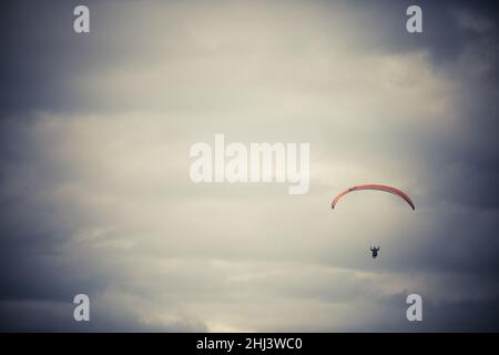 Bild eines Gleitschirms, der alleine fliegt, gegen einen grau bewölkten Himmel. Stockfoto