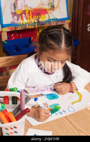 Bildung Vorschule 4-5-jährige Mädchen am Tisch sitzen Schreiben mathematische Gleichung auf ihre Zeichnung 0 + 1 = Halten Marker mit Stativ Griff Stockfoto