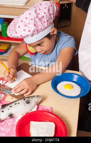 Bildung Vorschule 4-Jährige geben vor, spielen Mädchen Koch schreiben Lebensmittel bestellen Spielzeug Telefon am Ohr Stockfoto
