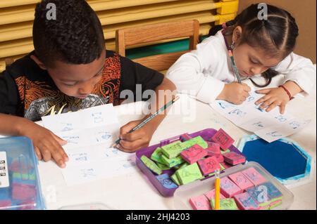 Bildung Vorschule 4-jährige Jungen und Mädchen sitzen nebeneinander Schreiben mit Bleistiften mit gegenüberliegenden Händen Stockfoto