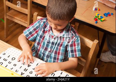 Bildung Vorschule 4-5 Jahre alten Jungen am Tisch sitzen spielen mit Alphabet Buchstaben Spiel Stockfoto