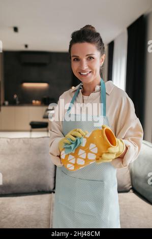 Eine Frau in Handschuhen, die eine orangefarbene Vase putzt Stockfoto