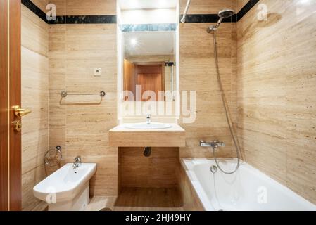 Badezimmer mit marmorgefliesten Wänden, Waschbecken, Spiegel, Badewanne und Bidet in einer Ferienwohnung Stockfoto