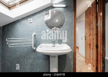 Toilette in einer Wohnung mit einer schrägen Decke mit blauen Kacheln und einer Kiefernholztür Stockfoto