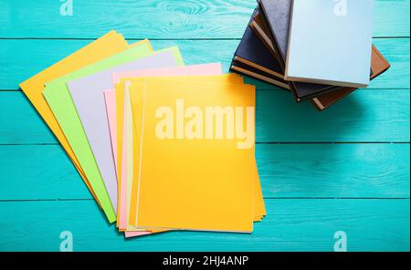 Farbenfrohe Papiere mit Platz zum Kopieren und viele Bücher auf blauem Holztisch. Stockfoto