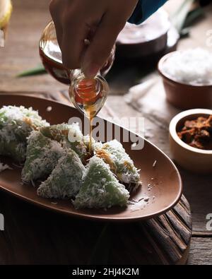 Lupis, indonesischer traditioneller Snack aus klebriges Reis, verpackt mit Bananenblatt, Shape Triangle serviert mit flüssigem Palmzucker und geriebener Kokosnuss Stockfoto