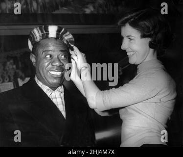 Der amerikanische Jazzmusiker Louis Armstrong hält auf dem Weg zurück in die USA am Flughafen Prestwick in Glasgow. Hier lässt er seine Baskenmütze vom 24-jährigen May Halliday ausziehen. 22nd. Dezember 1956. Stockfoto