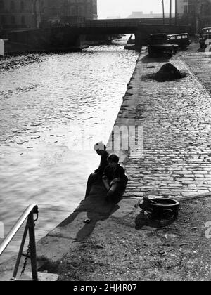 Newtown war ein Wohngebiet von Cardiff, Wales, das von der Mitte des 19. Jahrhunderts bis zum Abriss im Jahr 1970 existierte. Auf dem Bild am Wasser sitzen zwei Jungen im „Hinterhof“ von Newtown pensiv und beobachten das Spiel von Licht und Schatten auf dem Wasser. 28th. März 1956. Stockfoto