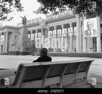 Ein Mann sitzt auf einer öffentlichen Bank auf einem verlassenen Platz in der sowjetischen Stadt Taschkent. Auf den Säulen vor ihm hängen Porträts von Mitgliedern des aktuellen sowjetischen Politbüros, flankiert von riesigen Bildern von Karl Marx (links) und Vladimir Lenin vom 1960. Mai Stockfoto