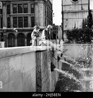 Zwei müde Angestellte des Versicherungsbüros waren auf dem Weg von der Stadt nach Hause. Als sie an St. Paul's vorbeikamen, schauten sie über den kühlen, einladenden Brunnen in einem monumentalen Garten. Es war zu viel, um Widerstand zu leisten, sie kletterten an die Wand, zogen ihre Schuhe und Socken aus, baumeln ihre heißen, schmerzenden Füße über den Brunnen und saßen dort zufrieden gleichgültig gegenüber staunenden Passanten. 26th. Juli 1956. Stockfoto