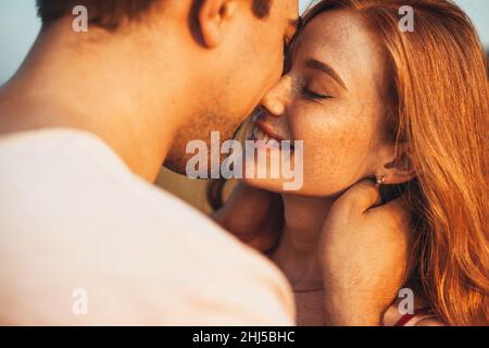 Nahaufnahme eines Mannes, der seine Freundin mit Sommersprossen küsst und vor einem hellen Hintergrund der Nachmittagssonne steht. Liebe liegt in der Luft. Nahaufnahme Porträt Stockfoto