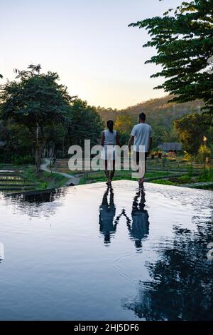 Ein Paar Männer und Frauen, die den Sonnenuntergang am Rande eines Pools mit Blick auf die Berge und Reisfelder von Nord-Thailand Mae Hong Son beobachten. Stockfoto