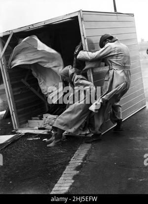 Sturmschaden. Ein Paar klammert sich verzweifelt an ihre umgekehrte Strandhütte in Littlehampton, um zu verhindern, dass sie weggeblasen wird. Littlehampton, West Sussex. 29th. Juli 1956. Stockfoto