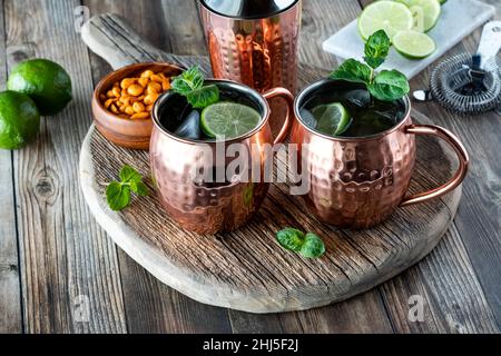 Frostige Moscow Mule Cocktails auf einem rustikalen Holzbrett serviert mit Erdnüssen. Stockfoto