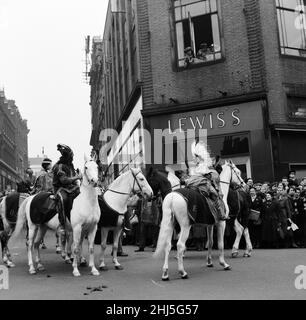 Cowboys und Indianer vom Billy Smarts Circus fahren in die Stadt und führen vor dem lokalen Geschäft Lewis's einen Laufkampf durch. Davy Crocket Smart bekämpft den Angriff von einem Fenster im Obergeschoss aus. Hanley, Staffordshire. 21st. März 1956. Stockfoto