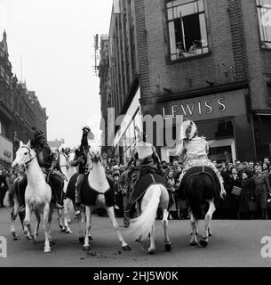 Cowboys und Indianer vom Billy Smarts Circus fahren in die Stadt und führen vor dem lokalen Geschäft Lewis's einen Laufkampf durch. Davy Crocket Smart bekämpft den Angriff von einem Fenster im Obergeschoss aus. Hanley, Staffordshire. 21st. März 1956. Stockfoto