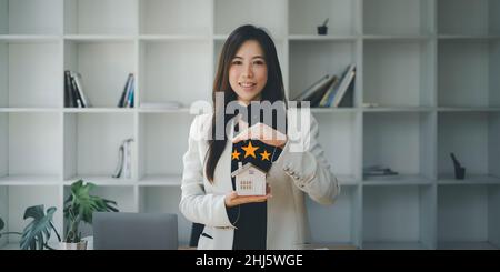 Asiatischer Versicherungsagent, der ein Handsymbol macht, um das Haus vor einem Unfall zu schützen. Immobilien- und Vertragskonzept.. Stockfoto