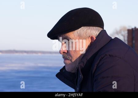 Porträt eines ernsthaft nachdenklichen und runzeligen Mannes im Alter, der im Winter draußen zur Seite schaut Stockfoto