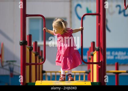 Lustiges kaukasisches kleines Mädchen von zwei Jahren, das auf dem Spielplatz zur Seite schaut Stockfoto