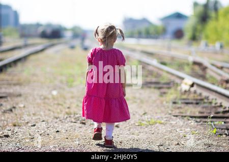 Das kleine Mädchen, das im Sommer allein auf Schienen auf der Eisenbahn herumläuft Stockfoto