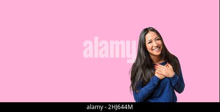 Junge Frau zeigt ihre herzlichen Dank und dank drückte ihre Hände an ihr Herz mit einem zufrieden Lächeln auf, isoliert auf rosa Stockfoto