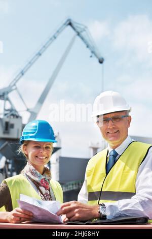 Der Mentor übergibt die Herrschaft. Zwei Hafenarbeiter, die Papierkram halten, während sie in der Werft stehen. Stockfoto