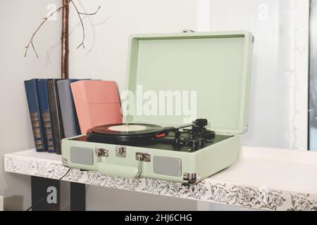 Retro-Stil Hause Vinyl-Plattenspieler oder Plattenspieler. Tragbares Gerät für LP-Disk hören. Retro-Musik. Vintage-Bücher auf einem Regal Stockfoto
