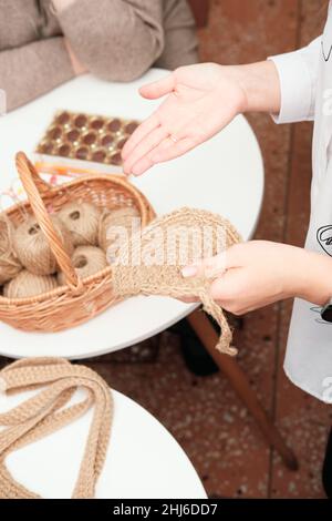 Frauenhänden mit Strickhäkchen, natürliche Materialien für ein gestricktes Projekt. Jutefaden für Nadelarbeit. Gemütliche handwerkliche Atmosphäre Stockfoto