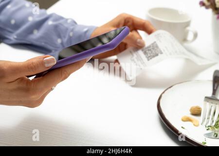Eine Frau scannt einen QR-Code mit einem Telefon in einem Café. Stockfoto