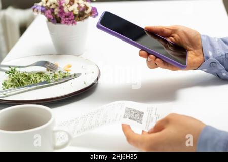 Eine Frau scannt einen QR-Code mit einem Telefon in einem Café. Stockfoto