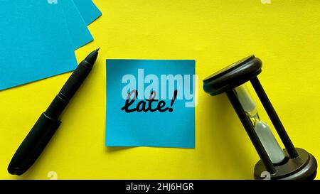 Draufsicht auf blaue Haftnotiz mit spätem Text. Mit Minutengläsern und gelbem Hintergrund. Geschäftskonzept. Stockfoto