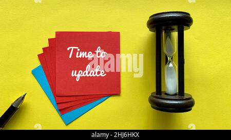 Draufsicht auf rote Haftnotiz mit Zeit zum Aktualisieren des Textes. Mit Minutengläsern und gelbem Hintergrund. Geschäftskonzept. Stockfoto