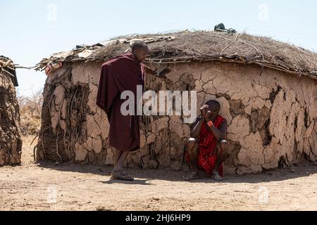 AMBOSELI-NATIONALPARK - 17. SEPTEMBER 2018: Maasai-Männer plaudern vor der Schlammhütte Stockfoto