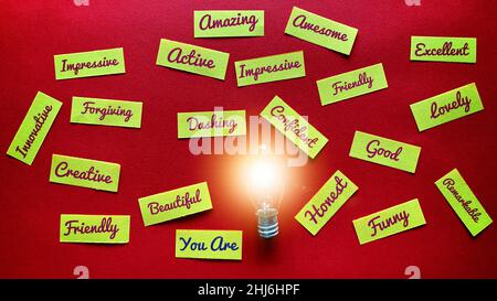 Draufsicht auf positive Formulierungen auf kleinen Papierstücken mit hellem, leuchtendem Lampenhintergrund. Motivationskonzept. Stockfoto