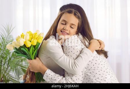 Das kleine Mädchen umarmt Mama, als sie am Muttertag ihren Strauß aus gelben Tulpen gibt Stockfoto