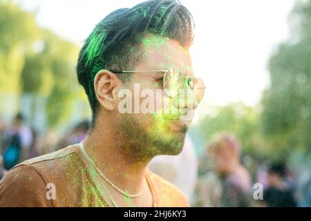 Schöner lächelnder Mann mit schwarzen Haaren und farbenfrohem Gesicht, der auf dem Holi-Farbfestival Spaß hat Stockfoto