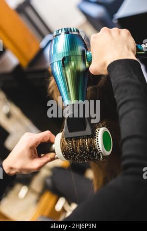 Friseurmeisterin trocknet die Haare des Mädchens mit einem Haartrockner und Kämmen nach dem Waschen im Schönheitssalon. Stockfoto