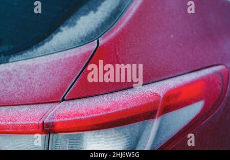 Rotes Auto bedeckt von Frost und Eis von weißem Schnee in der Wintersaison. Nahaufnahme der Rückseite des roten Autos, das auf dem Parkplatz im Freien geparkt ist. Kalt und gefroren Stockfoto