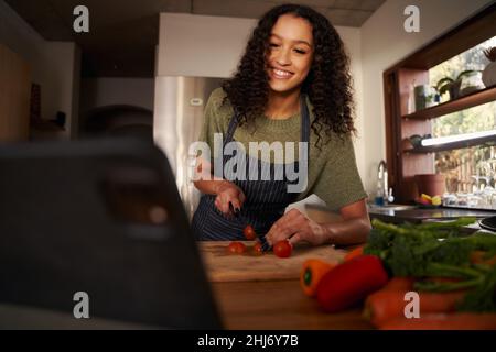 Afroamerikanische lächelnde Frau, die Gemüse hackt und Videos auf einem digitalen Tablet ansieht Stockfoto