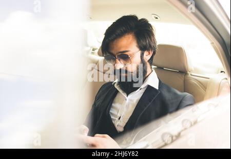 Stilvoller, hübscher indischer Geschäftsmann arbeitet auf dem Rücksitz des Autos. Sichere und komfortable Luxusreisen Stockfoto