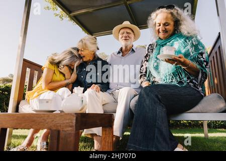 Gruppe älterer Freunde, die fröhlich lachen, während sie zusammen Tee trinken. Fröhliche ältere Freunde genießen ihren Sommerurlaub in einem Spa Resort. Senior CI Stockfoto