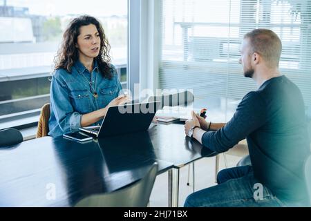 Weibliche Arbeitgeberin, die ein Bewerbergespräch führt. Geschäftsfrau, die einen jungen Mann für einen Job im Büro interviewt. Stockfoto