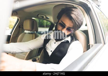 Stilvoller und erfolgreicher Inder in einem stilvollen Anzug, der ein Luxusauto fährt. Die besten Autos und Bedingungen für Ihr Unternehmen Stockfoto