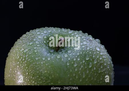 apfel mit Wassertropfen. Makroaufnahme eines frischen grünen Apfels, bedeckt mit sprudelnden Wassertropfen vor dunklem Hintergrund Stockfoto