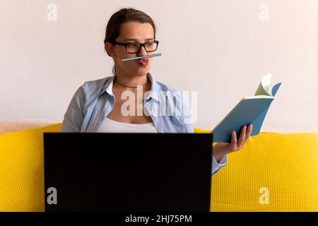 Erfolgreiche hart arbeitende Geschäftsfrau mit Laptop. Junge Ledy in der Schwangerschaft hält Bleistift mit Lippen und Nase Arbeit Papierkram aus der Ferne über das Internet Stockfoto
