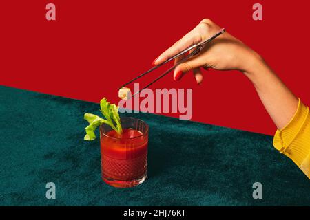 Weibliche Hand machen Cocktail Bloody mary isoliert auf hellgrünen und roten Neon-Hintergrund. Konzept des Geschmacks, alkoholische Getränke. Vintage-Stil Stockfoto